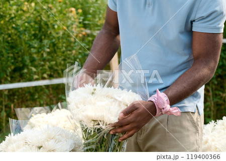 Close up of unrecognizable African American man arranging bouquet of white flowers at market sale copy space 119400366