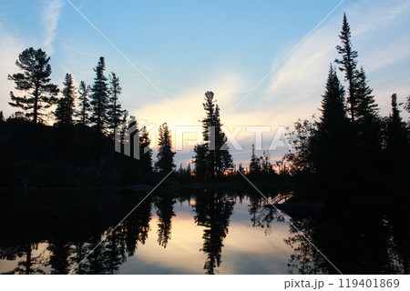 Sunset on lake in forest. Silhouettes of trees are reflected in calm water Sunset on lake in forest. Silhouettes of trees are reflected in calm water 119401869