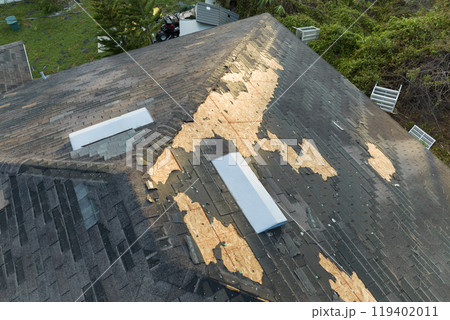 Damaged house roof with missing shingles after hurricane Ian in Florida. Consequences of natural disaster Damaged house roof with missing shingles after hurricane Ian in Florida. Consequences of natural disaster 119402011