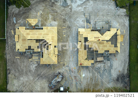 Aerial view of builders working on unfinished residential house with wooden roof frame structure under construction in Florida suburban area 119402521