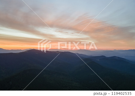 Aerial view of dark mountain hills with bright sunrays of setting sun at sunset. Hazy peaks and misty valleys in evening 119402535