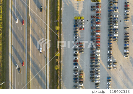 Aerial view of dealership parking lot with many brand new cars for sale near wide american highway. Development of US automotive industry concept Aerial view of dealership parking lot with many brand new cars for sale near wide american highway. Development of US automotive industry concept 119402538