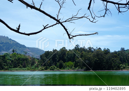 Serene Dieng landscape with a lake, mountains, and a tree branch against a blue sky. Serene Dieng landscape with a lake, mountains, and a tree branch against a blue sky. 119402895