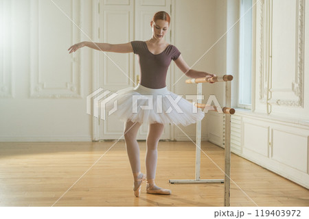Young ballerina in tutu skirt stretching practicing ballet positions dancing near ballet barre in dance class. Young classical dancer woman in dance studio. Ballet class training Ballet school concept Young ballerina in tutu skirt stretching practicing ballet positions dancing near ballet barre in dance class. Young classical dancer woman in dance studio. Ballet class training Ballet school concept 119403972