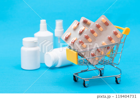 Pills and Capsules in Shopping Cart on Blue Background 119404731