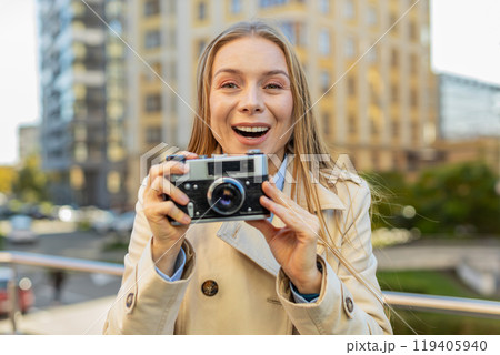 Happy mature woman tourist exploring city making pictures on retro vintage camera on city street 119405940