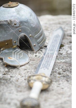 Medieval Helmet and Sword Resting on Stone Surface, Historical Weaponry 119407372