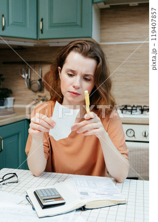 woman pays bills online, sits in kitchen with receipts and calculator. Online banking woman pays bills online, sits in kitchen with receipts and calculator. Online banking 119407857