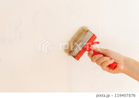 Person is holding brush with glue on background of light wall. apply thick wallpaper glue. Person is holding brush with glue on background of light wall. apply thick wallpaper glue. 119407876