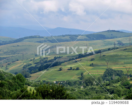 Mountain slopes with power lines and green rural fields and trees Mountain slopes with power lines and green rural fields and trees 119409088