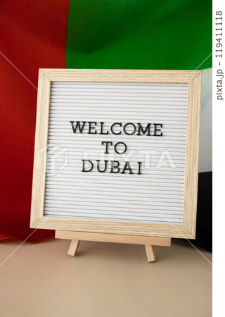 Frame text WELCOME TO DUBAI on background of waving UAE flag made from silk. United Arab Emirates flag with concept of tourism and traveling. Inviting greeting card, advertisement 119411118