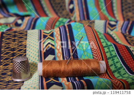 Brown Thread With Thimble on Colorful Vintage Fabric 119411758