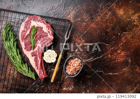 Raw uncooked dry aged beef tomahawk or rib eye steak. Dark background. Top view. Copy space Raw uncooked dry aged beef tomahawk or rib eye steak. Dark background. Top view. Copy space 119413092