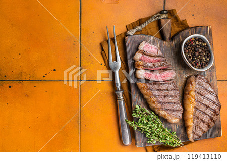 BBQ Roast brazilian Picanha steak, cup rump beef meat steak on a wooden serving board. Orange background. Top view. Copy space 119413110