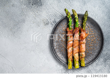 Plate with pork bacon wrapped asparagus on grey table. White background. Top view. Copy space Plate with pork bacon wrapped asparagus on grey table. White background. Top view. Copy space 119413180
