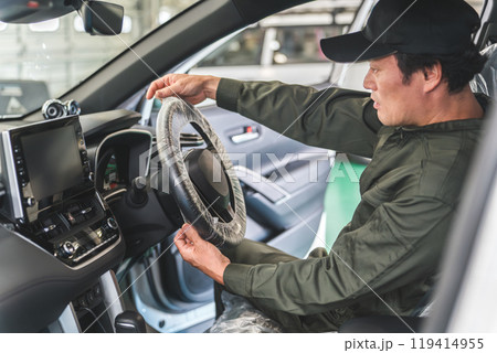 整備工場に入庫したお客様の車に養生のためにハンドルカバーをする整備士の男性 整備工場に入庫したお客様の車に養生のためにハンドルカバーをする整備士の男性 119414955