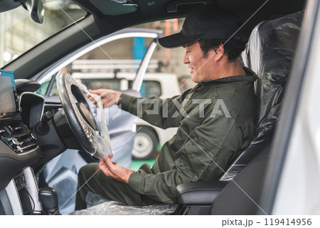 整備工場に入庫したお客様の車に養生のためにハンドルカバーをする整備士の男性 119414956