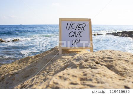 Never give up symbol. White Blackboard with Concept words Never give up. Beautiful sea background. Business and Never give up concept. Copy space. 119416686