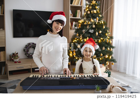 Mother and daughter playing piano beside Christmas tree Mother and daughter playing piano beside Christmas tree 119419425