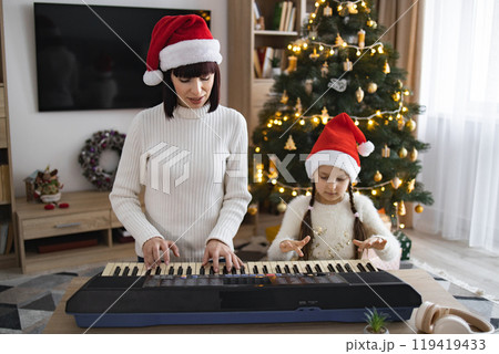 Mother and daughter play keyboard and sing Christmas carols together Mother and daughter play keyboard and sing Christmas carols together 119419433