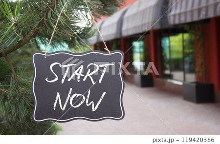 Start now symbol. Concept words Start Now on black chalk blackboard. Beautiful background with shop and tree. Business and Start now concept. Copy space. Start now symbol. Concept words Start Now on black chalk blackboard. Beautiful background with shop and tree. Business and Start now concept. Copy space. 119420386