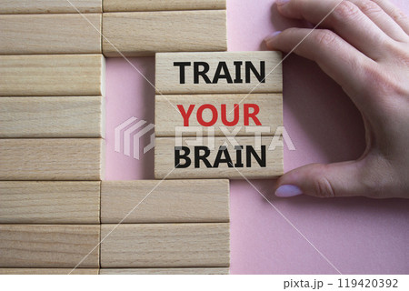 Train Your Brain symbol. Concept words Train Your Brain on wooden blocks. Beautiful pink background. Doctor hand. Healthcare and Train Your Brain concept. Copy space. 119420392