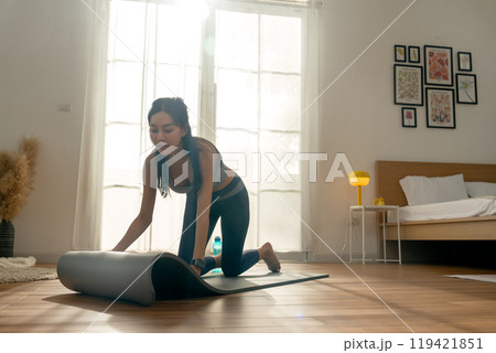 Close up pretty Asian woman with exercise clothes lay out a yoga mat to prepare for exercise in front of warm light throgh glass door. Close up pretty Asian woman with exercise clothes lay out a yoga mat to prepare for exercise in front of warm light throgh glass door. 119421851