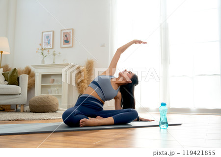 Pretty Asian woman with exercise clothes do yoga posture with raise her right arm over and cross her head in room with day light Pretty Asian woman with exercise clothes do yoga posture with raise her right arm over and cross her head in room with day light 119421855