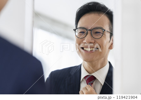 鏡を見てネクタイを整える笑顔の0代後半のビジネスマン 119421904