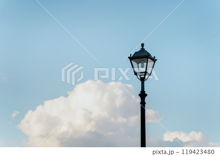 An elegant street lamp stands against a backdrop of lush clouds and a clear blue sky. 119423480