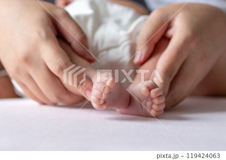 A mother gentle hands cradle her baby tiny feet, capturing a tender moment of warmth and love, with soft, delicate toes resting in her caring embrace. 119424063