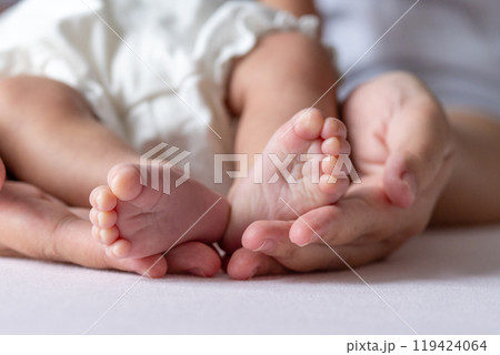 A mother gentle hands cradle her baby tiny feet, capturing a tender moment of warmth and love, with soft, delicate toes resting in her caring embrace. 119424064