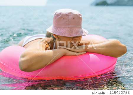 A woman is laying on a pink inflatable raft in the ocean. The scene is peaceful and relaxing, with the woman enjoying the water and the sun. A woman is laying on a pink inflatable raft in the ocean. The scene is peaceful and relaxing, with the woman enjoying the water and the sun. 119425788