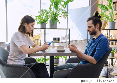 Young couple sitting at table in coffee shop, using smartphones 119427327
