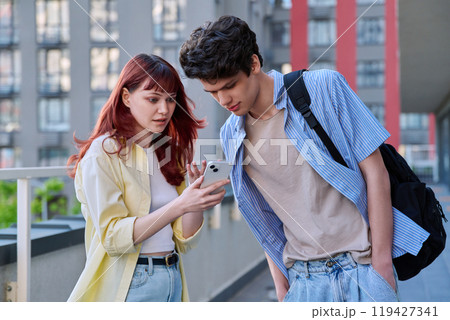 Friends young guy and girl college students talking looking at smartphone together, outdoor Friends young guy and girl college students talking looking at smartphone together, outdoor 119427341