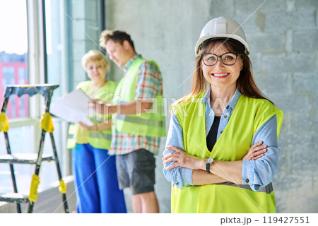 Woman in safety vest hard hat with crossed arms on new residential or commercial real estate site Woman in safety vest hard hat with crossed arms on new residential or commercial real estate site 119427551