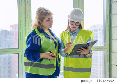 Two female industrial workers at construction site discussing work Two female industrial workers at construction site discussing work 119427552