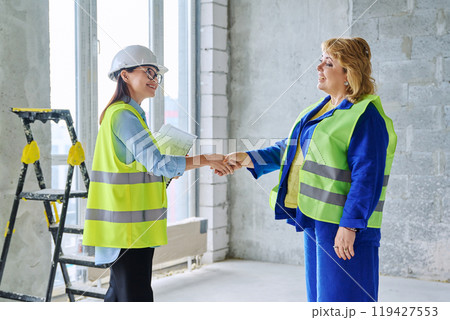 Two female colleagues in protective vests shaking hands at construction site 119427553