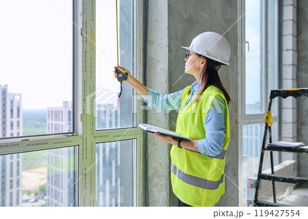 Woman in safety vest hard hat with tape measure on new residential or commercial real estate site Woman in safety vest hard hat with tape measure on new residential or commercial real estate site 119427554