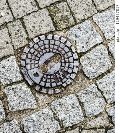 Closed sewer manhole on an old paved road.Top view 119427817