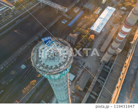 Construction site of a power plant a high chimney.Dangerous work at height.A renovation is smokestack.Contractor repairing a chimney at a highrise.Workers in a hard hat.Dangerous work at the daytime. 119431847