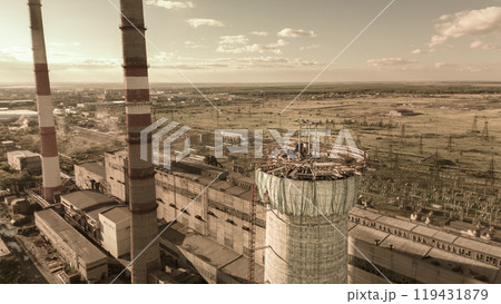 Construction site of a power plant a high chimney.Dangerous work at height.A renovation is smokestack.Contractor repairing a chimney at a highrise.Workers in a hard hat.Dangerous work at the daytime. Construction site of a power plant a high chimney.Dangerous work at height.A renovation is smokestack.Contractor repairing a chimney at a highrise.Workers in a hard hat.Dangerous work at the daytime. 119431879