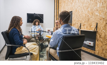 Small team having a focused meeting in a private office with a TV screen on the wall. 119433402