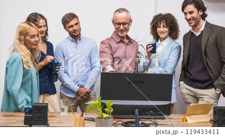 Happy mature male manager discussing strategy on computer with team in office Happy mature male manager discussing strategy on computer with team in office 119433411