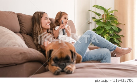 Smiling mother and girl on sofa watching TV at home Smiling mother and girl on sofa watching TV at home 119433700