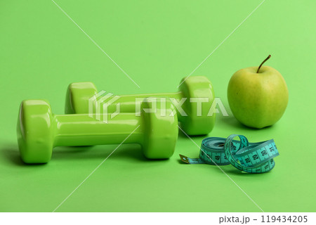 Dumbbells in bright green color, twisted measure tape and fruit Dumbbells in bright green color, twisted measure tape and fruit 119434205