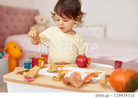happy little child girl painting autumn leaves. baby girl drawing leaves in yellow and orange paint happy little child girl painting autumn leaves. baby girl drawing leaves in yellow and orange paint 119434318