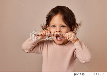 cute child girl bites fruit pastille on beige background. healthy baby food. cute child girl bites fruit pastille on beige background. healthy baby food. 119434363