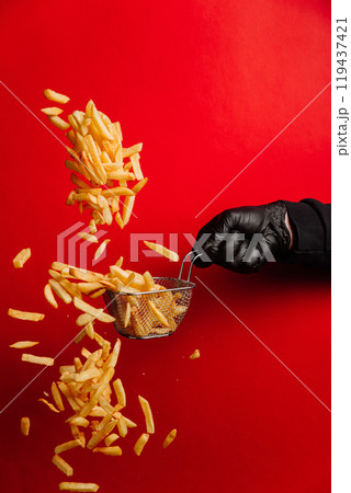 Dynamic shot of flying French fries falling from a basket against a bold red background Dynamic shot of flying French fries falling from a basket against a bold red background 119437421