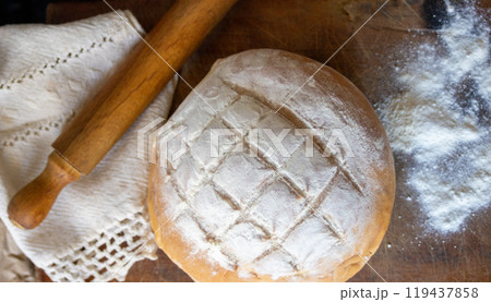 Country bread on wooden table next to a rolling pin. 119437858